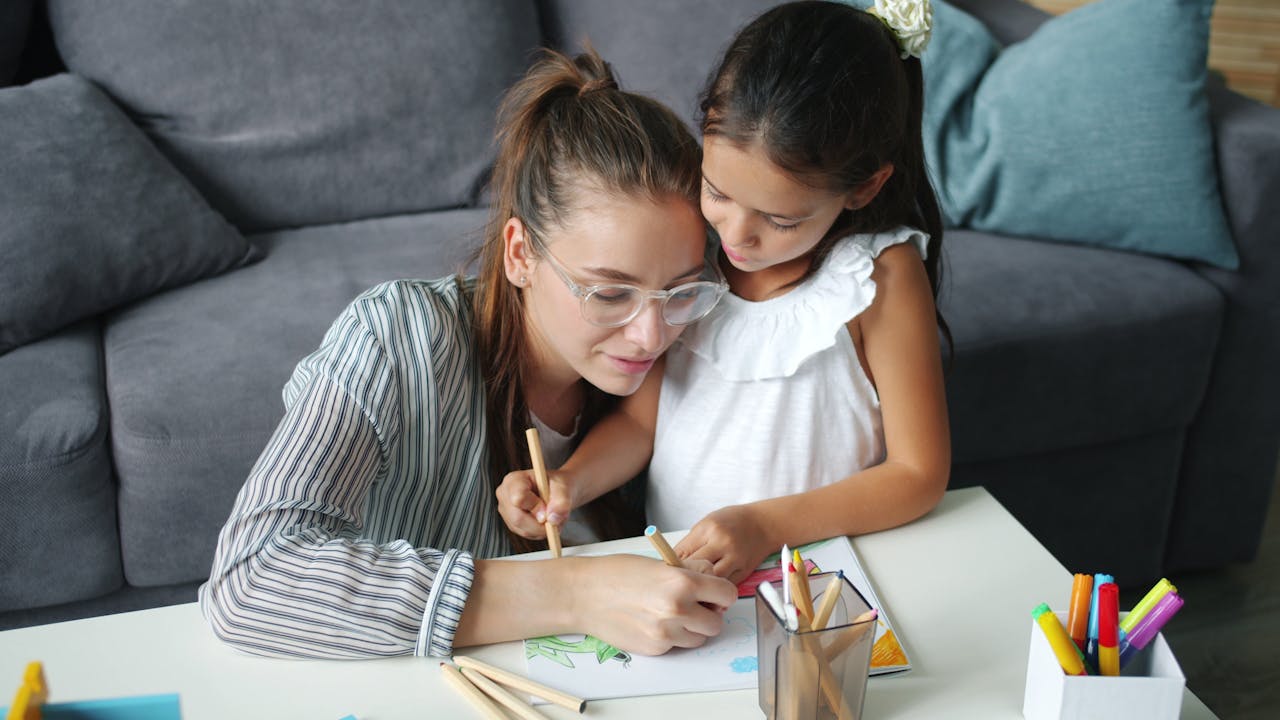 A mother and daughter engage in a drawing activity in a cozy living room setting.
